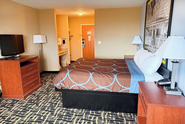 A hotel room with a bed, a TV, a desk, and a bathroom visible through an open door.