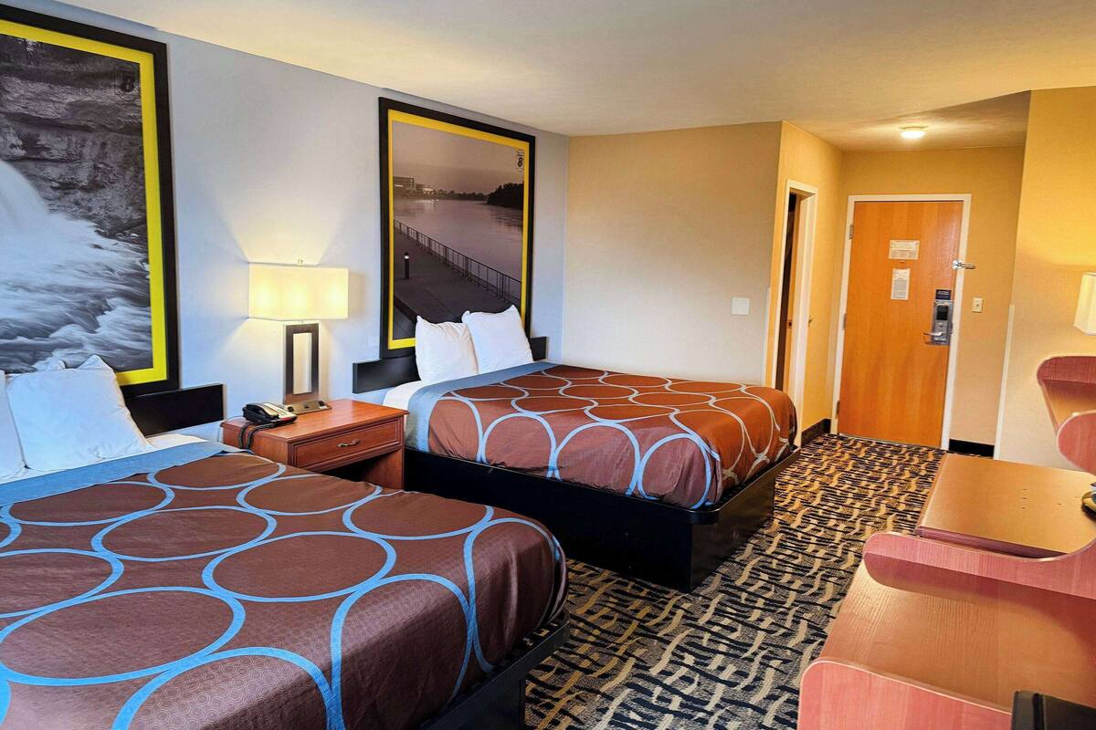 Ein Hotelzimmer mit zwei Betten, einem Schreibtisch, einem Stuhl, einer Lampe und einer Tür.