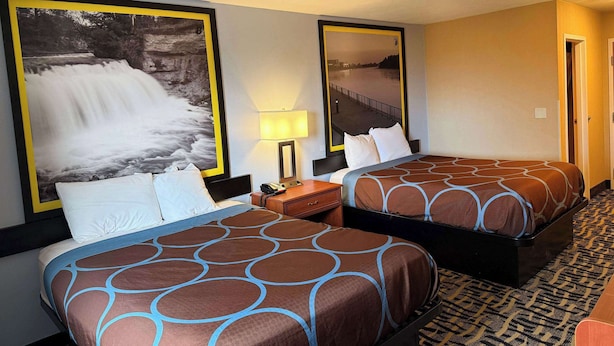 Habitación de hotel con dos camas, una mesita de noche con lámpara y un cuadro grande con una cascada.