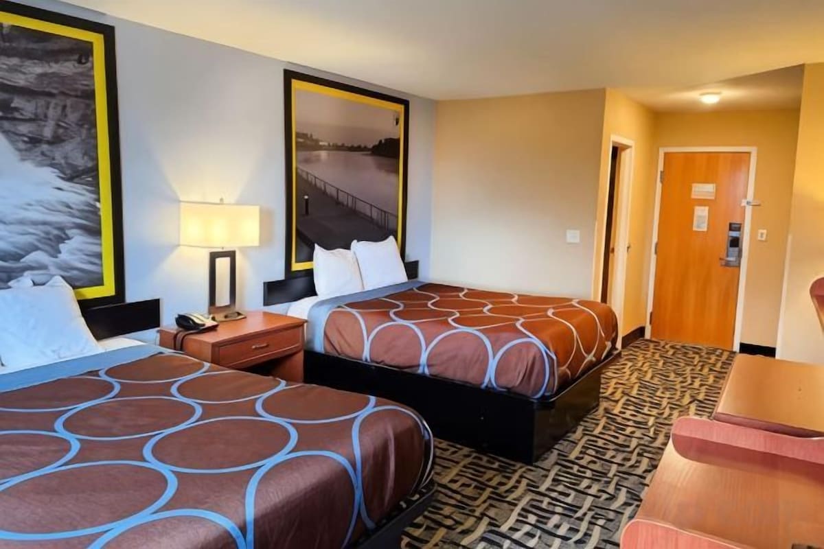 Una habitación de hotel con dos camas, un escritorio, una silla, una lámpara y una puerta.