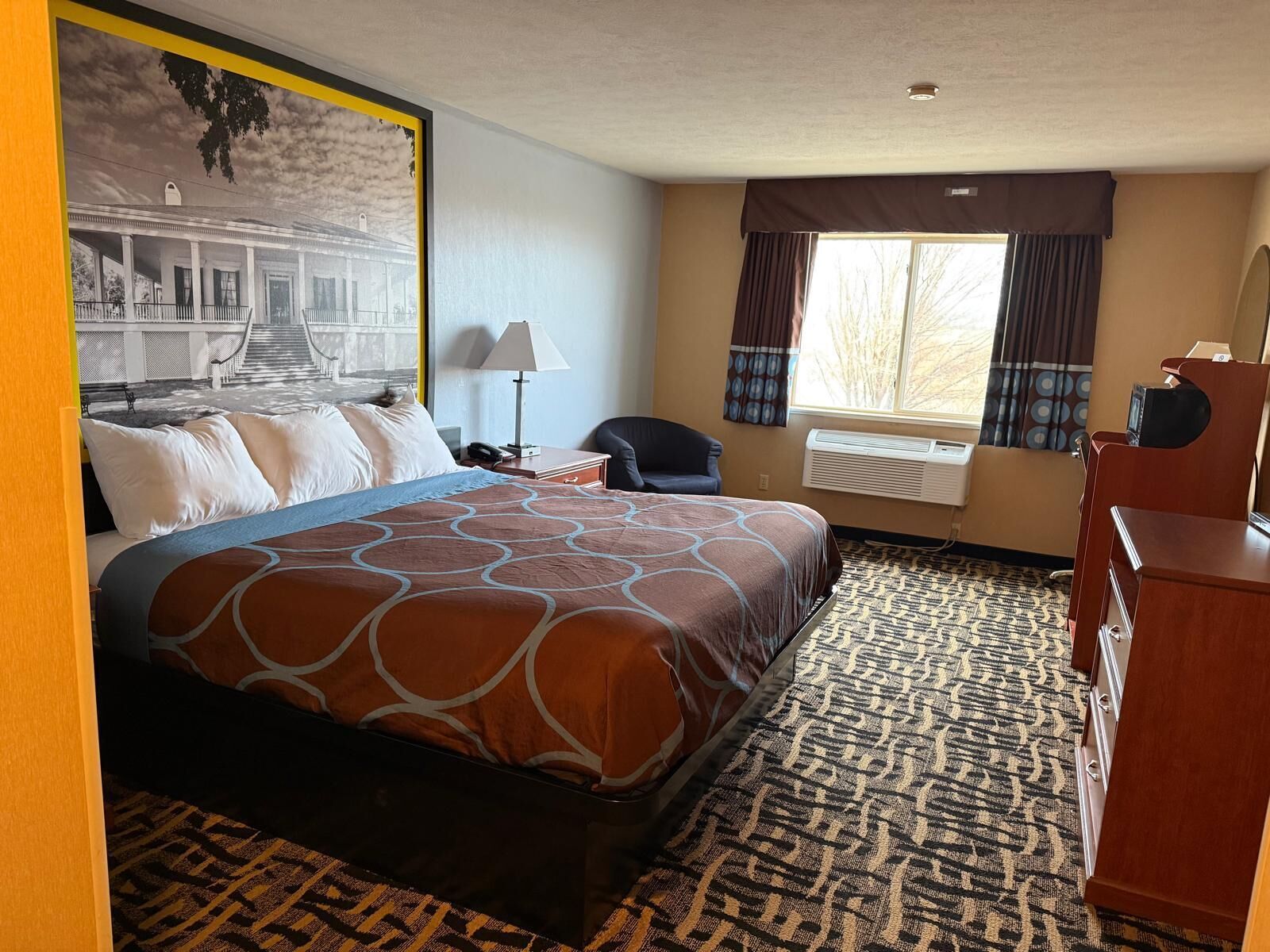 A hotel room with a large bed, a desk, a chair, and a window with curtains.