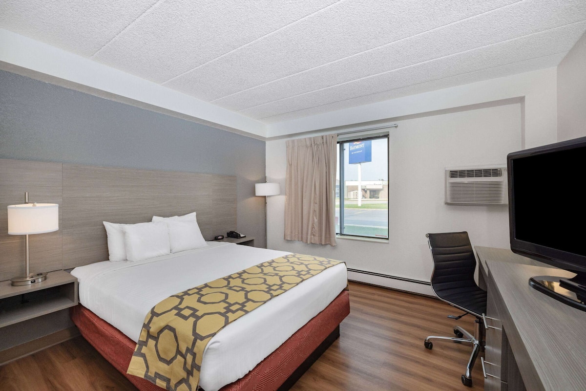 A hotel room with a bed, a desk, a chair, a TV, a lamp, and a window with curtains.