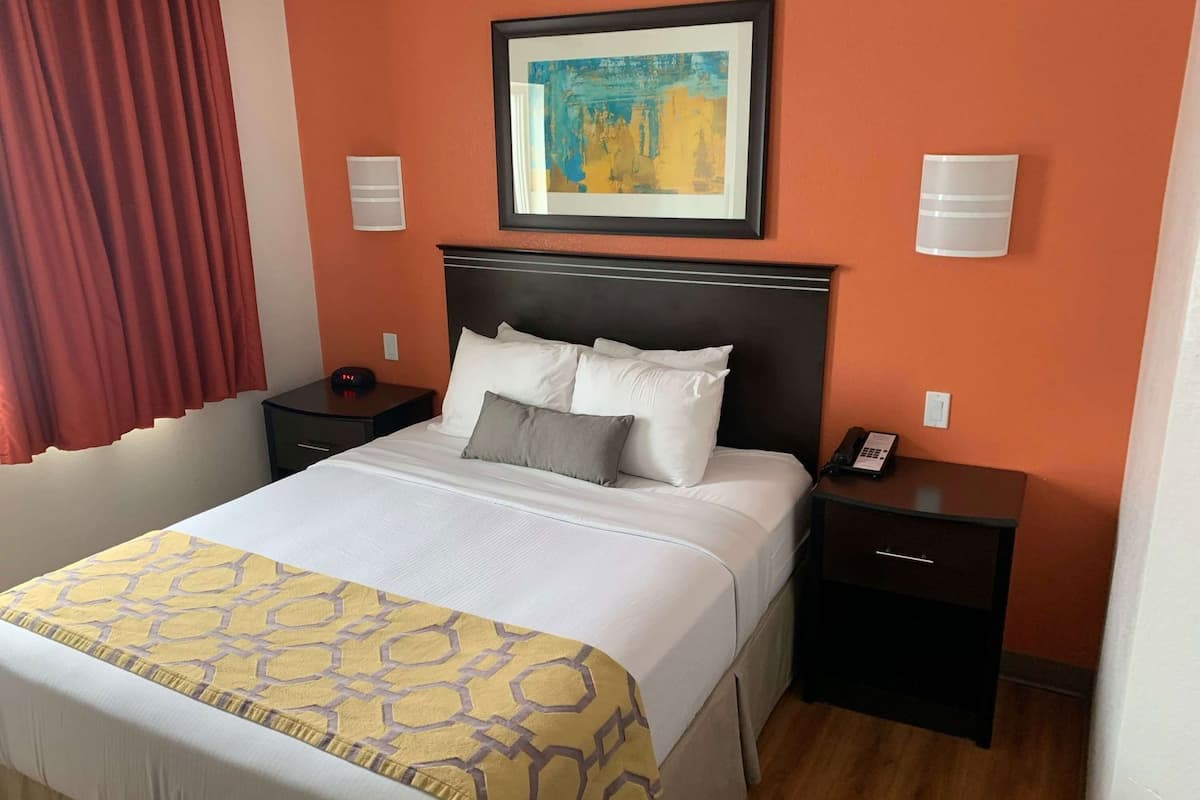 A hotel room with a bed, two bedside tables, a nightstand, a painting, and a telephone.