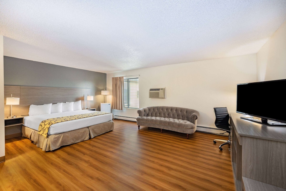 A hotel room with a bed, a sofa, a desk with a TV, and a window with curtains.