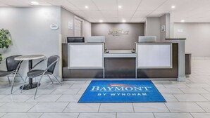 A reception area with a Baymont by Wyndham sign, two reception desks, a small round table with chairs, and a blue carpet with the hotel name. - Baymont by Wyndham Gillette (Gillette)