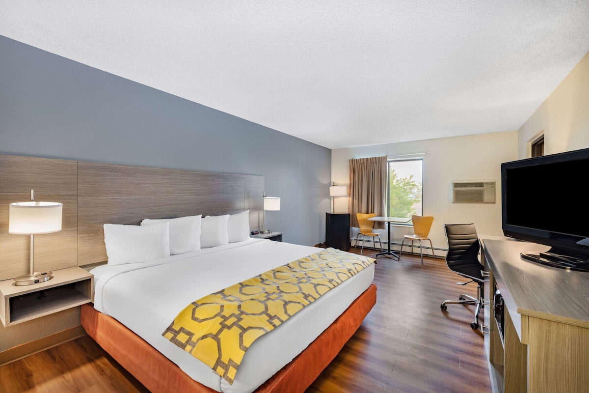 A hotel room with a large bed, a desk with a TV, a chair, and a window with curtains.
