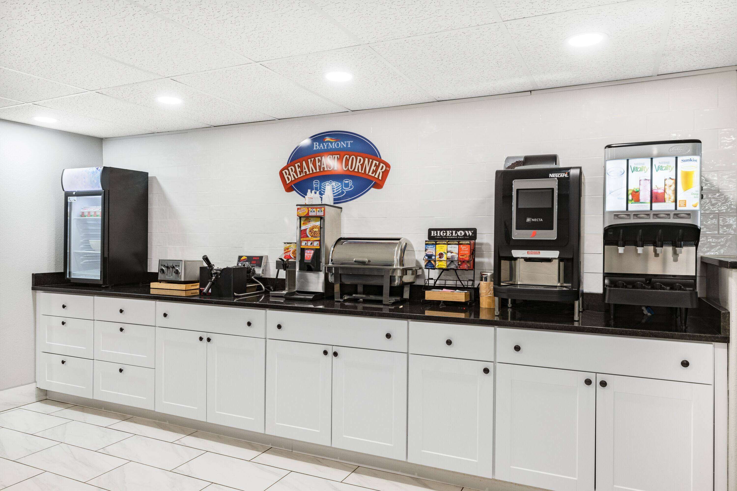 Un comptoir de petit-déjeuner orné d’une enseigne Baymont, avec une machine à café, une cafetière Bigelow et une machine à café Nescafé.
