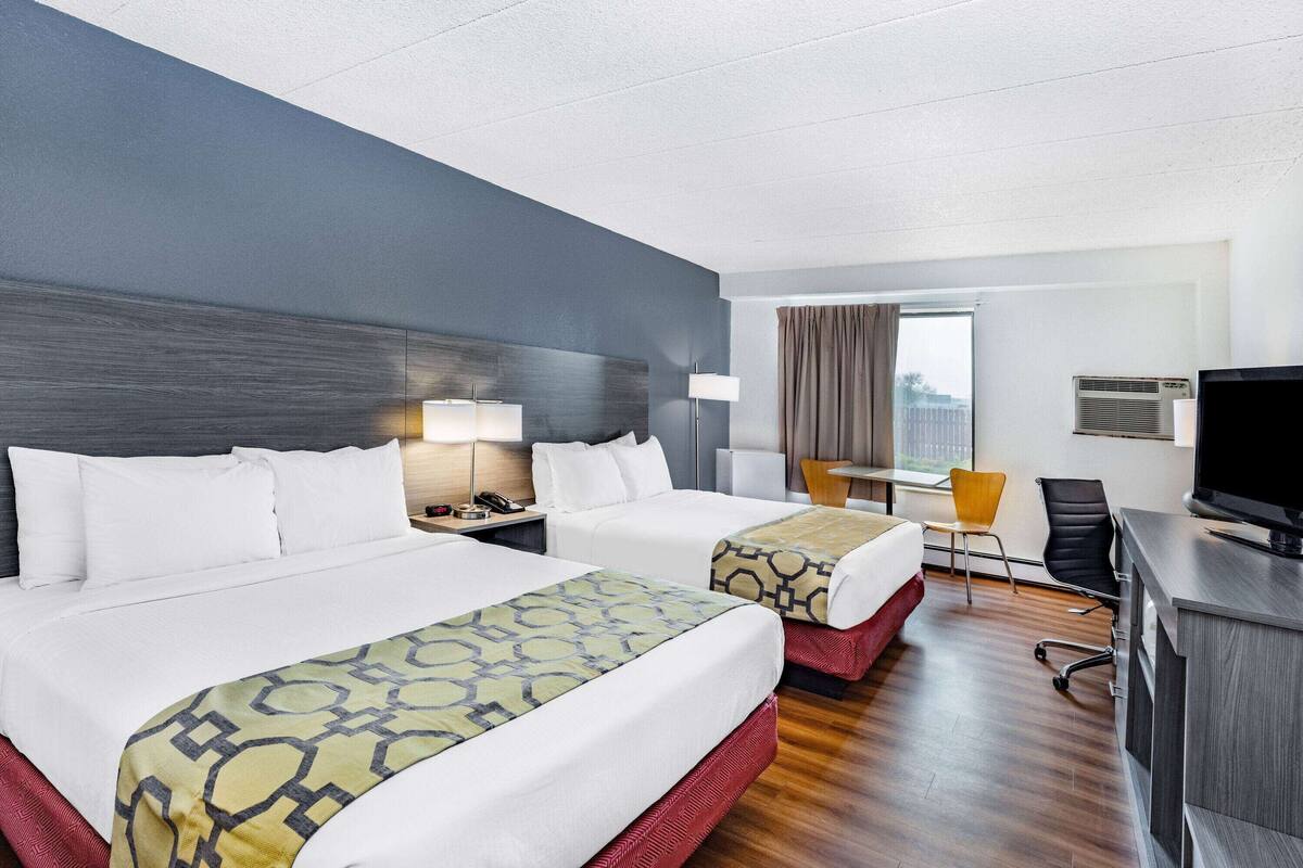 A hotel room with two beds, a desk, a chair, a TV, and a window with curtains.