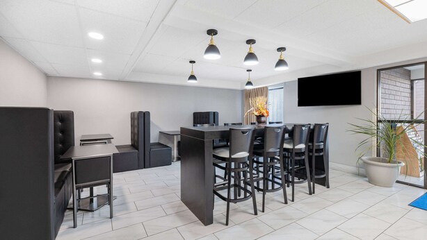 A modern office space with a dining area, black chairs, a central table, and a mounted TV. - Baymont by Wyndham Gillette (Gillette)