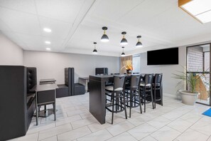 A modern office space with a dining area, black chairs, a central table, and a mounted TV.