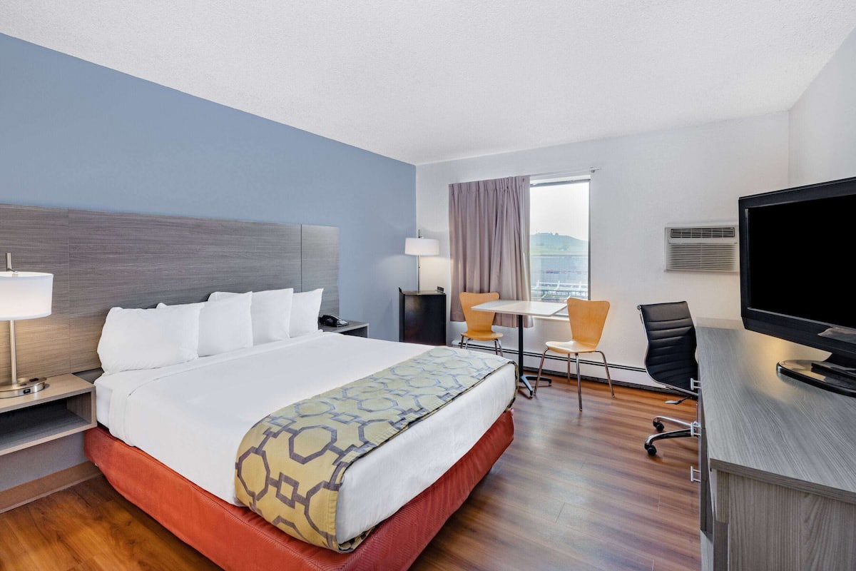 A hotel room with a bed, a desk, a chair, a TV, and a window with curtains.