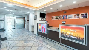 A hotel reception area with a tiled floor, a reception desk, a vending machine, and a wall with framed pictures. - Motel 6 Junction City, KS (Junction City)