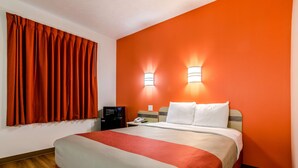 A hotel room with a bed, a nightstand, a telephone, and a wall-mounted light fixture. - Motel 6 Kearney, NE (Kearney)