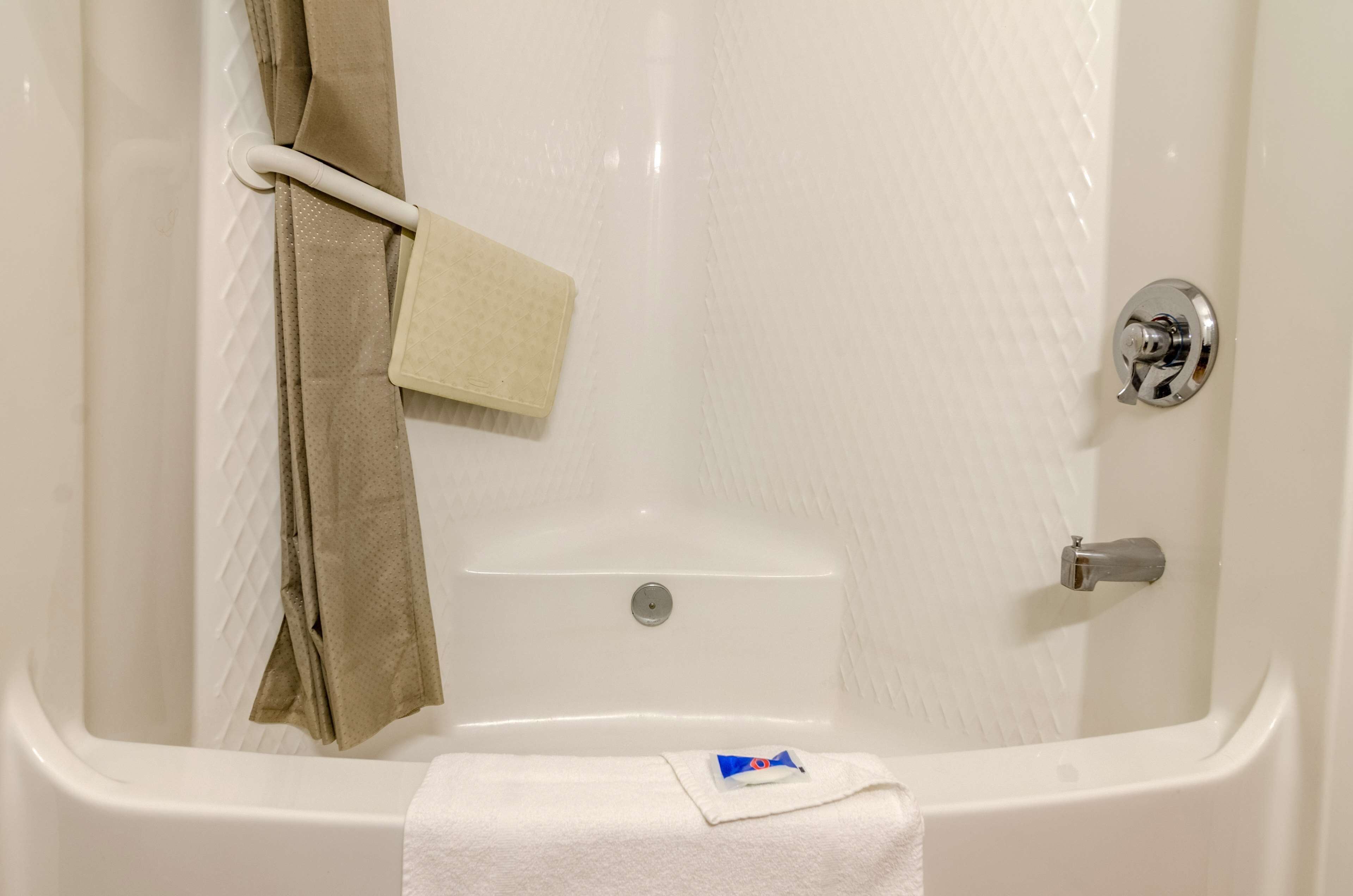 A white bathtub with a shower curtain, a towel, and a small bottle on the floor.
