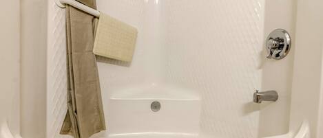 A white bathtub with a shower curtain, a towel, and a small bottle on the floor.