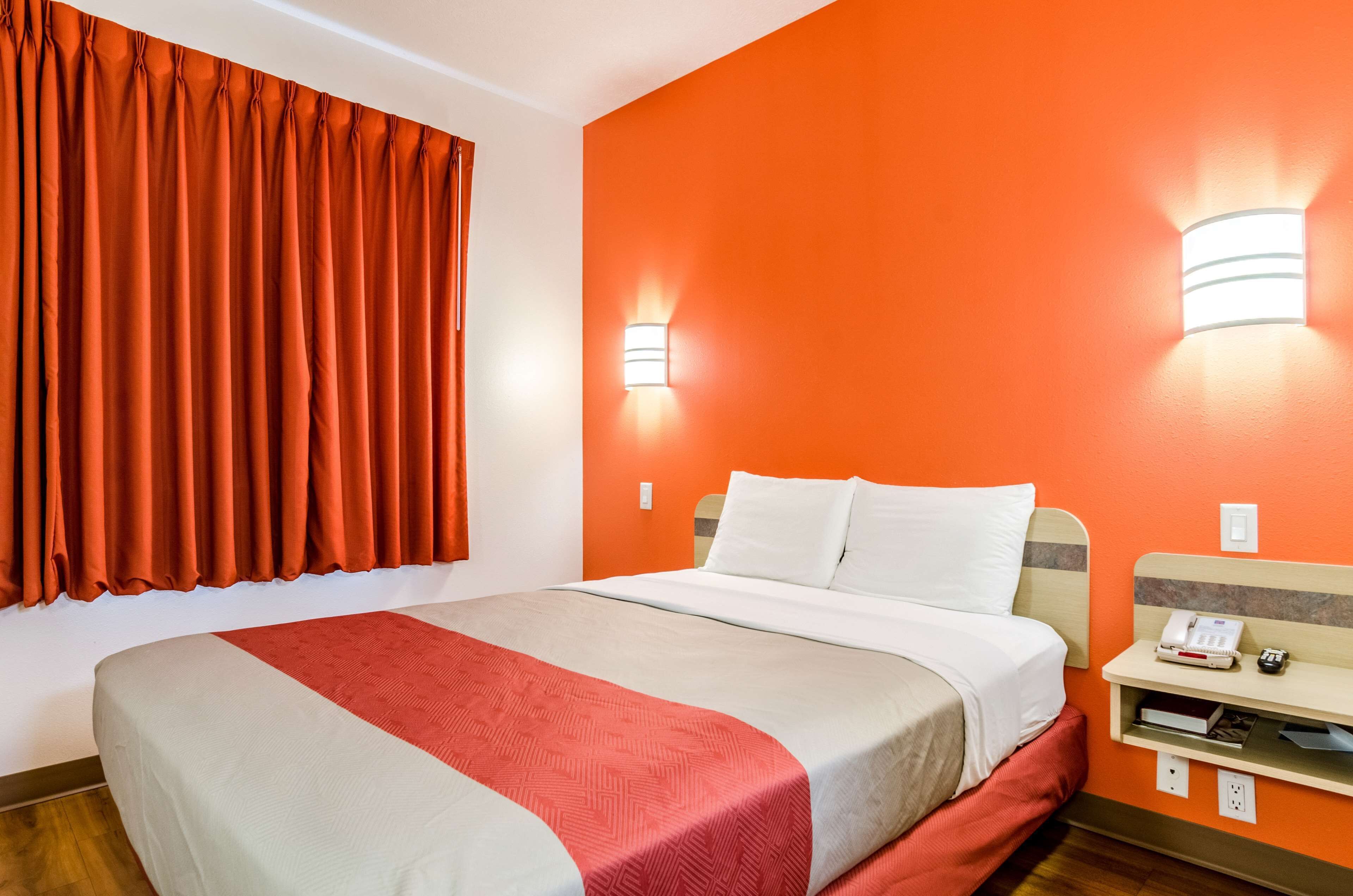 A hotel room with a bed, a nightstand, and a wall-mounted light fixture.