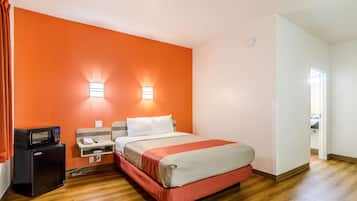 Une chambre d’hôtel avec un lit, un petit bureau doté d’une lampe, un four à micro-ondes et un rideau rouge.