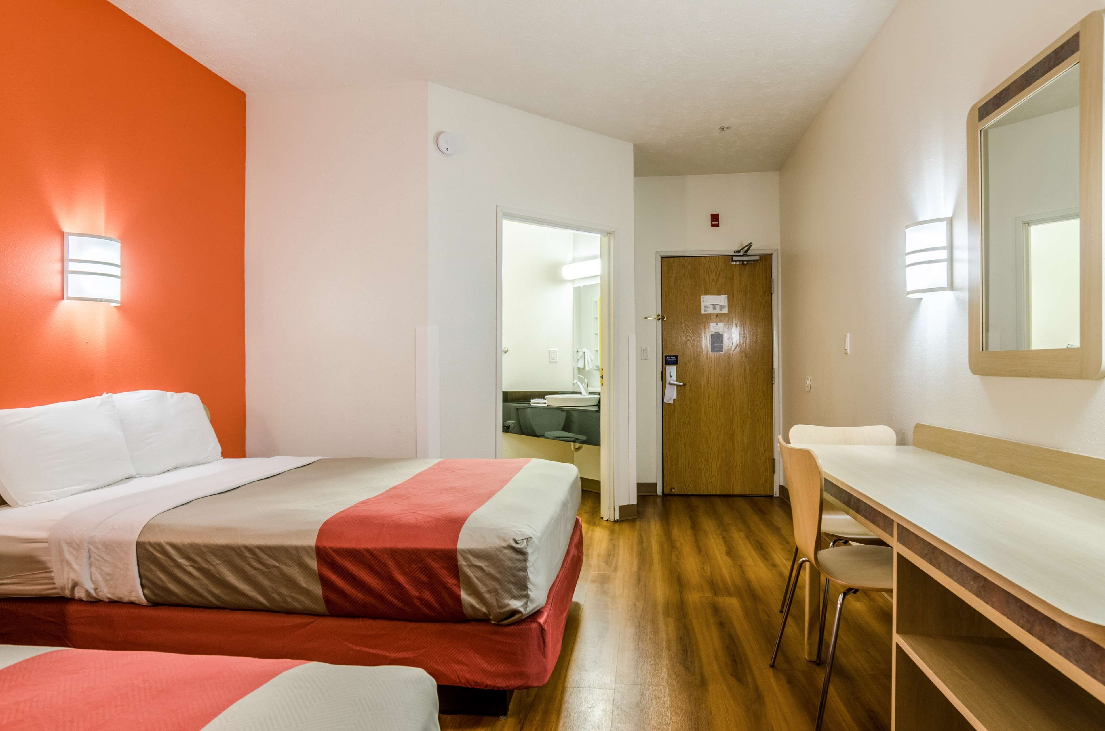 A hotel room with two beds, a desk, and a mirror.