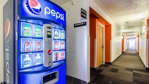 A hallway with a Pepsi vending machine, an elevator sign, and a carpeted floor. - Motel 6 Kearney, NE (Kearney)