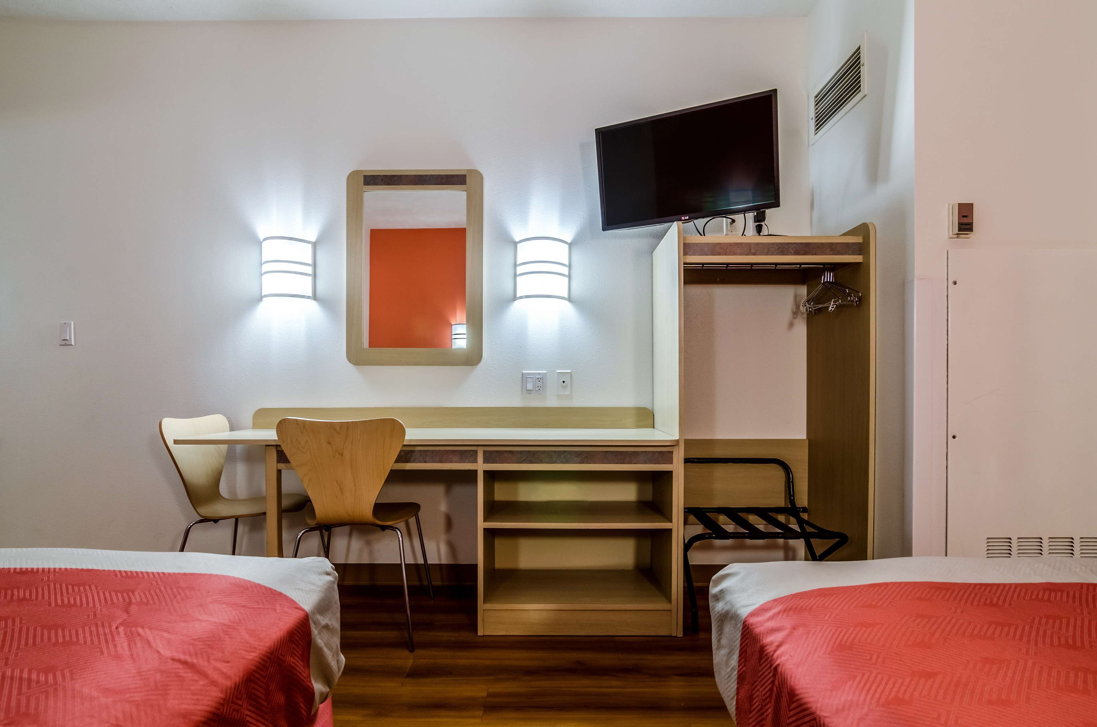 A hotel room with two beds, a desk with a chair, a television, a mirror, and a wardrobe.