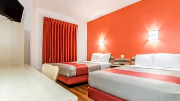 Ett hotellrum med två sängar, ett träbord, en tv och röda gardiner.