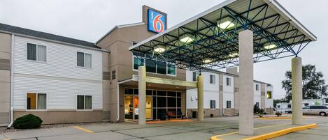 Ein Motel mit überdachter Eingangsparte, Parkplatz und einem Schild, das es als Motel 6 kennzeichnet.
