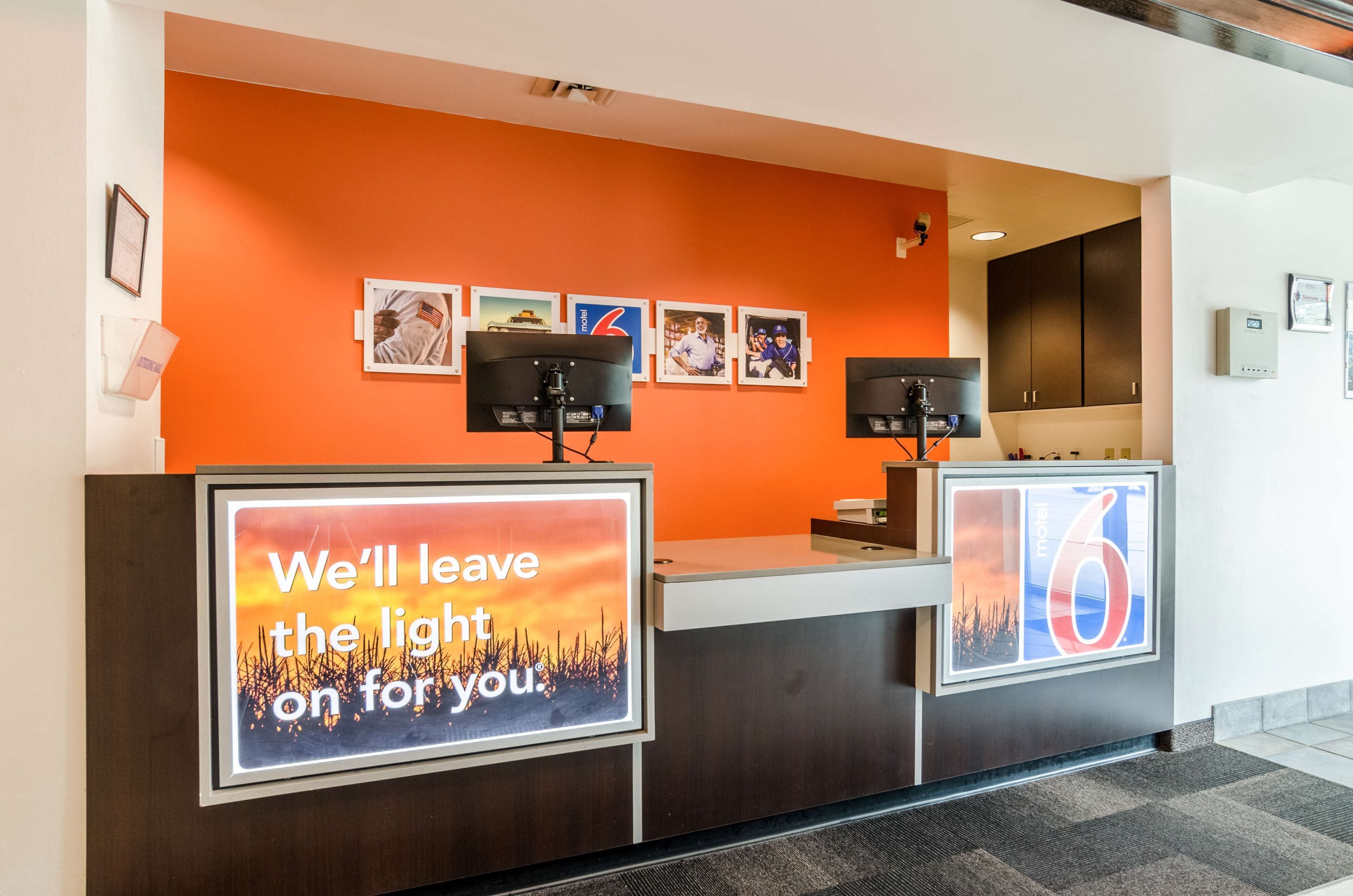 A hotel reception desk with an orange wall, framed pictures, and a large illuminated sign.