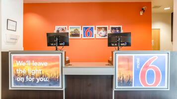Un mostrador de recepción con una pared de color naranja brillante, cuadros enmarcados y dos monitores.