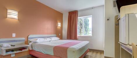 A hotel room with a bed, bedside table, lamp, window, and a built-in TV.