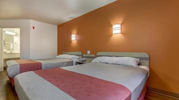 Quarto de hotel com duas camas, banheiro visível por uma porta aberta e luminárias fixadas na parede.