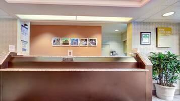 A reception desk with a brown counter, framed pictures on the wall, and a potted plant to the right.