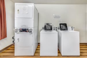 Uma fileira de máquinas de lavar roupa brancas num espaço com soalho de madeira e cortina castanha.