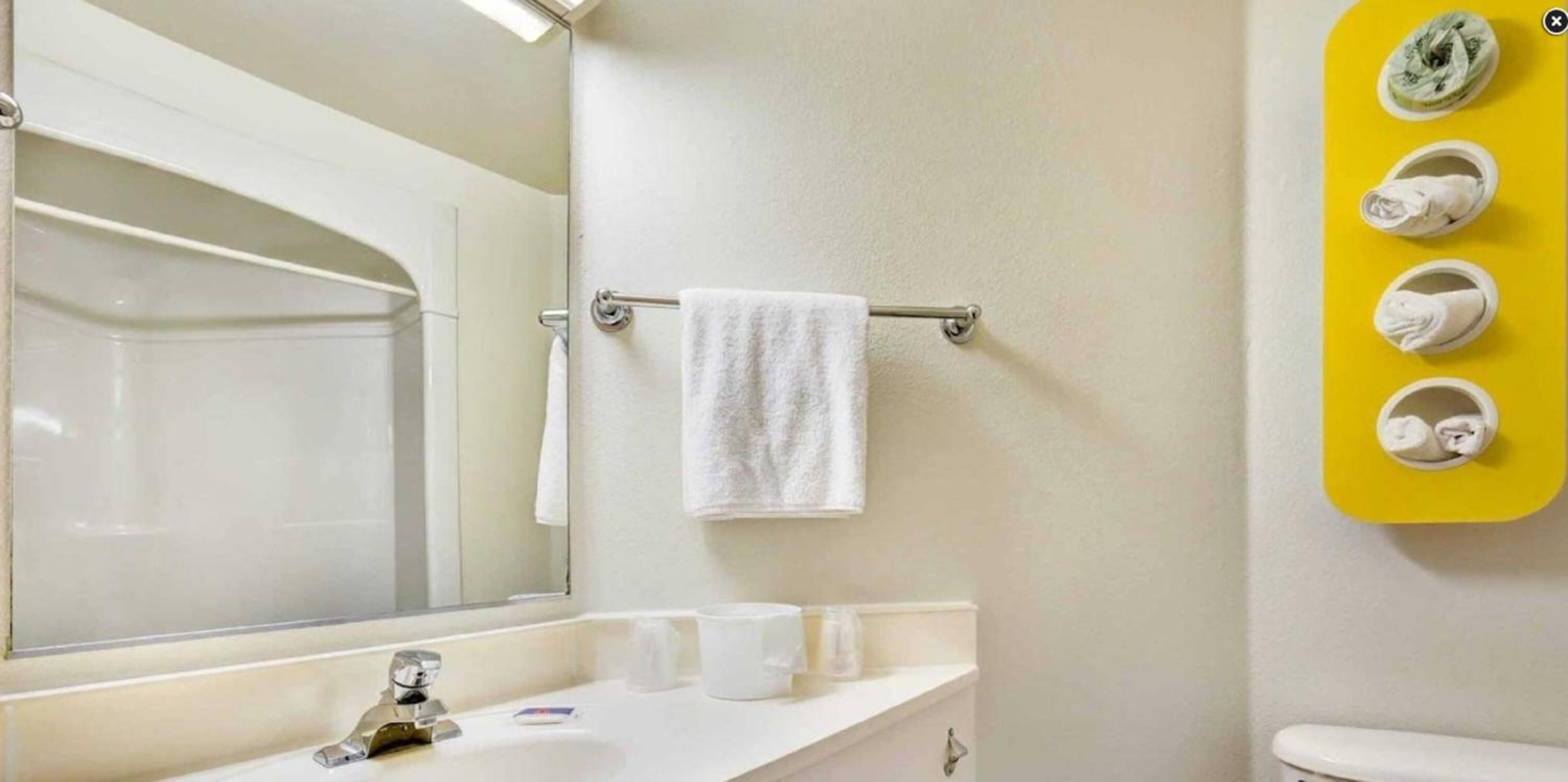 A bathroom with a white sink, a mirror, a towel rack with a white towel, and a yellow towel rack with multiple towels.