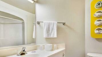 A bathroom with a white sink, a mirror, a towel rack with a white towel, and a yellow towel rack with multiple towels.