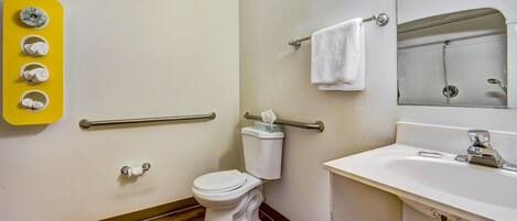 A bathroom with a toilet, sink, mirror, towel rack, and a yellow wall-mounted dispenser.