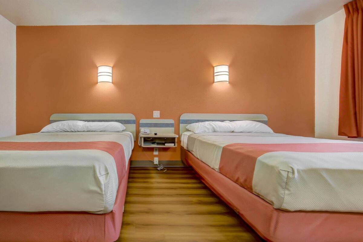 Une chambre d’hôtel avec deux lits, chacun équipé d’un oreiller et d’une tête de lit. Deux lampes murales sont fixées au-dessus des lits.