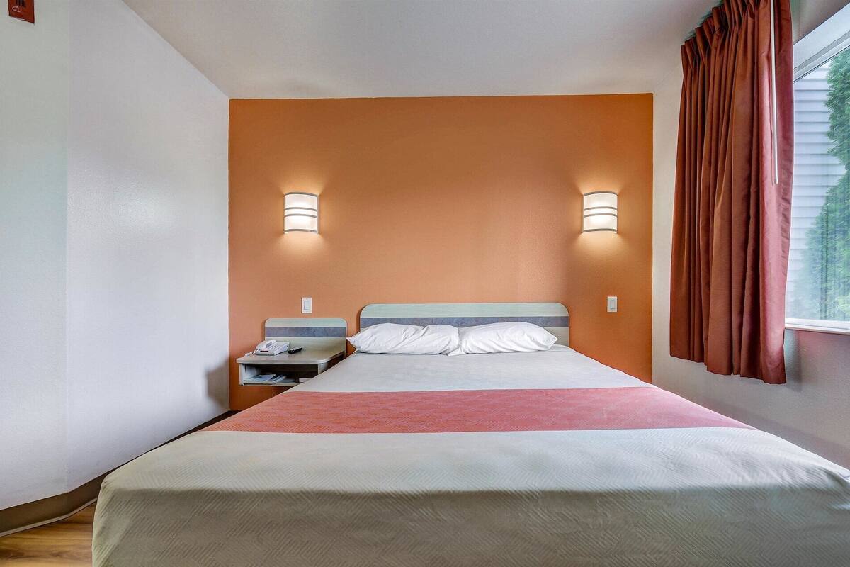 Une chambre d’hôtel avec un lit, une table de chevet, une lampe et une fenêtre avec des rideaux.