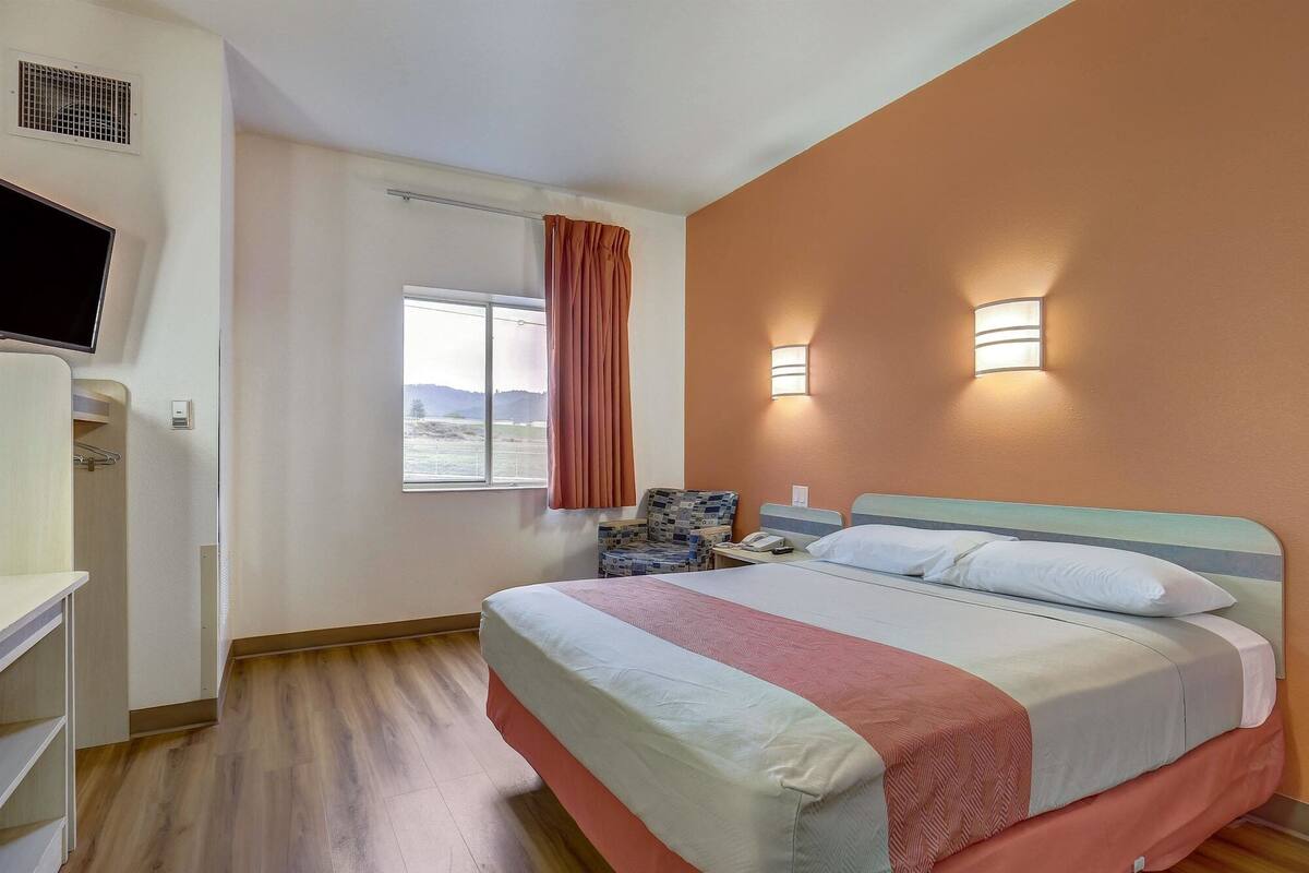Une chambre d’hôtel avec un lit, une chaise, une télévision et une fenêtre avec des rideaux.