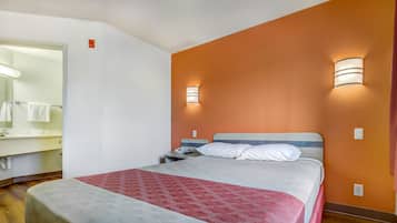 Habitación de hotel con cama, mesita de noche, teléfono, espejo y baño visible a través de una puerta abierta.