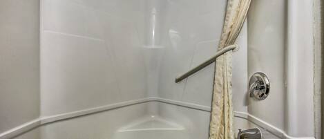 A corner of a bathroom with a bathtub, a shower curtain rod, and a faucet.