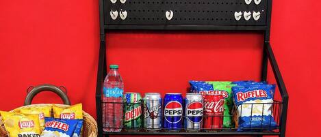 Exhibición de aperitivos y bebidas en un mercado, con diversas opciones de bocadillos, papas fritas y refrescos.