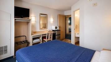 A hotel room with a bed, a desk, a chair, a microwave, a TV, and a wardrobe.