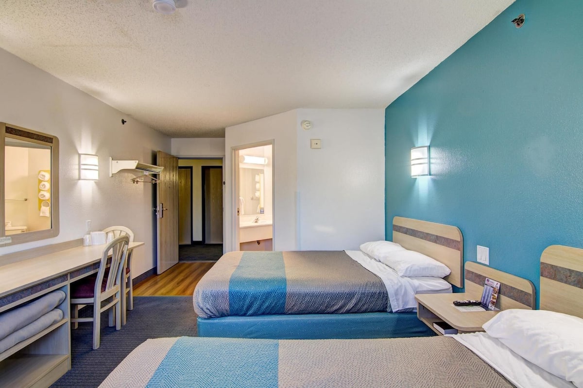 A hotel room with two beds, a desk, a chair, and a mirror.