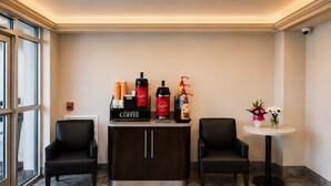 A reception area with a coffee station, two chairs, a small table with flowers, and a fire alarm on the wall. - Econo Lodge Menomonie (Menomonie)