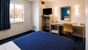 A hotel room with a bed, desk, chair, TV, and a window with curtains. - Econo Lodge Menomonie (Menomonie)