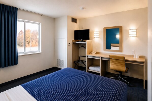 A hotel room with a bed, desk, chair, TV, and a window with curtains. - Econo Lodge Menomonie (Menomonie)