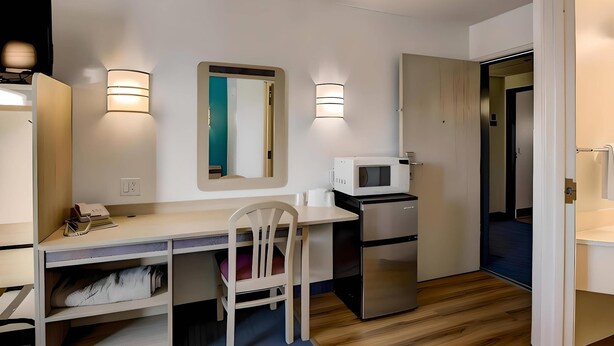 A compact kitchenette with a microwave, refrigerator, and a small dining table with a chair. There are two wall-mounted lights and a mirror above the table. - Econo Lodge Menomonie (Menomonie)