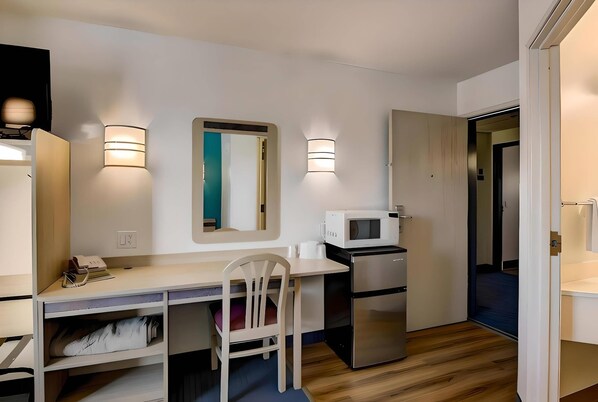 A compact kitchenette with a microwave, refrigerator, and a small dining table with a chair. There are two wall-mounted lights and a mirror above the table. - Econo Lodge Menomonie (Menomonie)
