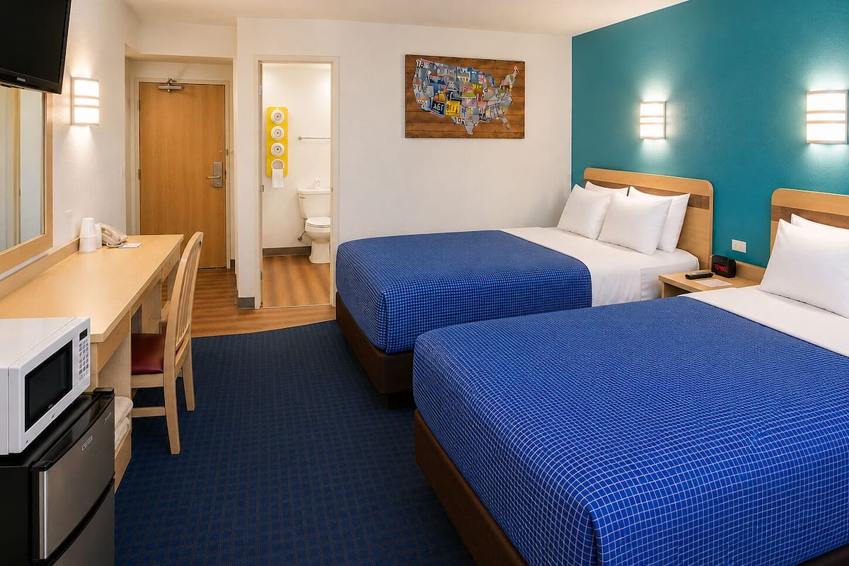 A hotel room with two beds, a desk, a microwave, and a television.