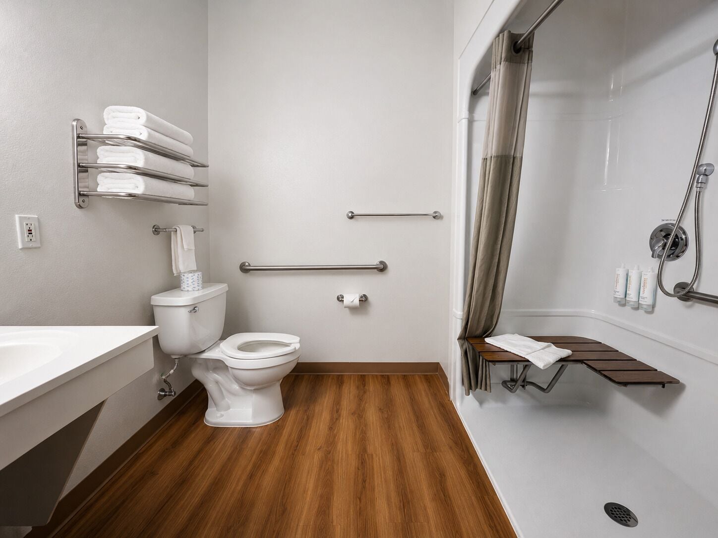 Un baño moderno con inodoro, bidé y zona de ducha, que incluye barras de apoyo y un perchero para toallas.